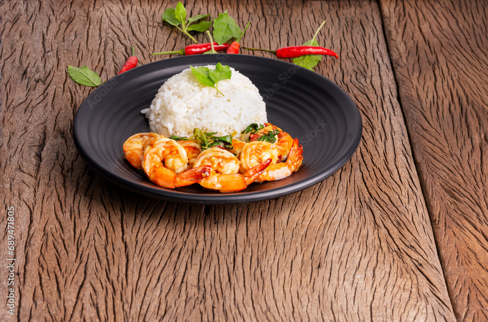Stir-fried shrimp with basil Thai street food, arranged on a black plate Spicy Thai food placed on a wooden table. Top view with space to copy text.