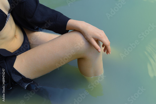 Part of the body, leg and arm of a young woman in a dark dress sitting in the water