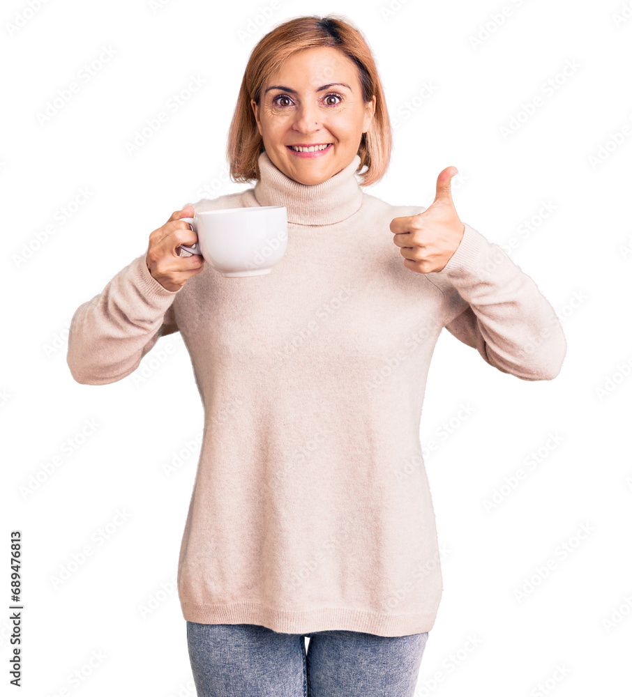 Young blonde woman holding coffee smiling happy and positive, thumb up doing excellent and approval sign Young blonde woman holding coffee smiling happy and positive, thumb up doing excellent and approval sign