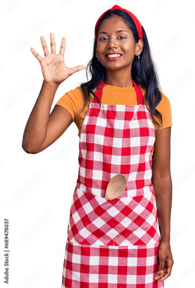Young indian girl wearing professional baker apron showing and pointing up with fingers number five while smiling confident and happy. Young indian girl wearing professional baker apron showing and pointing up with fingers number five while smiling confident and happy.