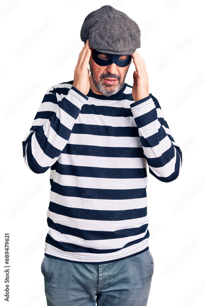 Middle age handsome man wearing burglar mask with hand on head for pain in head because stress. suffering migraine. Middle age handsome man wearing burglar mask with hand on head for pain in head because stress. suffering migraine.