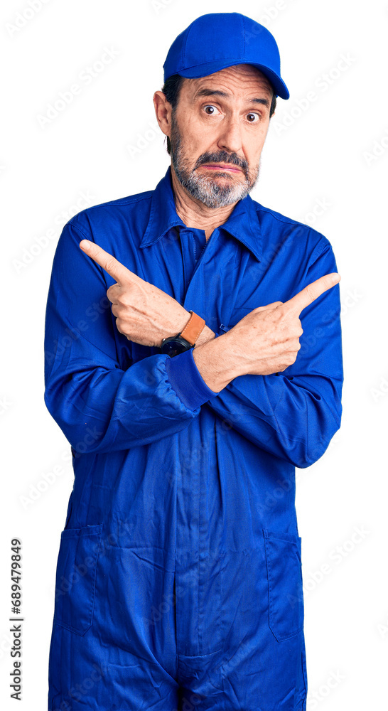 Middle age handsome man wearing mechanic uniform pointing to both sides with fingers, different direction disagree Middle age handsome man wearing mechanic uniform pointing to both sides with fingers, different direction disagree