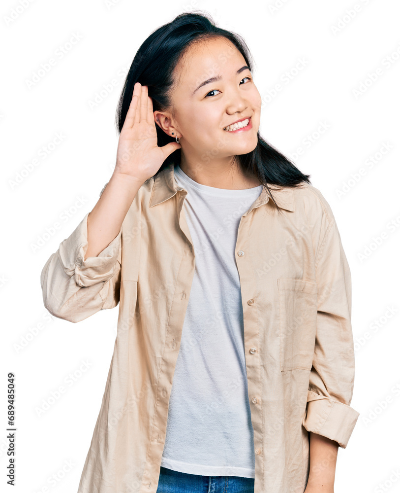 Young chinese woman wearing casual white t shirt and jacket smiling with hand over ear listening an hearing to rumor or gossip. deafness concept. Young chinese woman wearing casual white t shirt and jacket smiling with hand over ear listening an hearing to rumor or gossip. deafness concept.