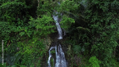Small waterfall flowing on cliff on mountainside in the middle of tropical forest with aerial view from drone.