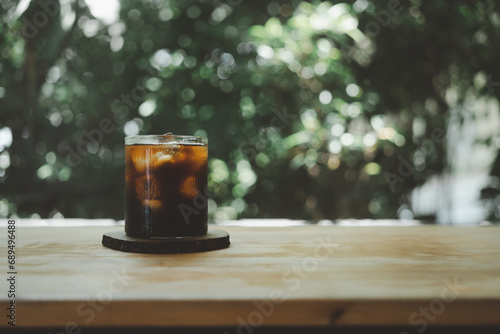 Cold black coffee with ice cubes on a wood table against nature background. Cold Brew. Summer drinks. photo