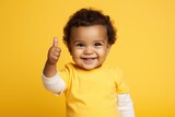 Portrait of a cute african american baby boy showing thumbs up over yellow background, a toddler giving a thumbs up on yellow background, AI Generated