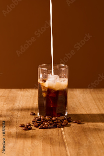 A stream of milk is pouring from above into a cup of black coffee on a wooden table with a brown background. Art space for food and beverage advertising.