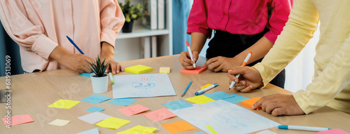 Group of young business group brainstorms ideas on colorful sticky notes. A portrait of startup group planing marketing strategy while writing down on sticky note at office meeting room. Variegated.