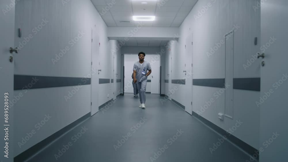 African American health care specialist in uniform walks medical center corridor. Patient greets with medical personnel in hospital hallway. Multi ethnic doctors and nurses work in clinic. Dolly shot. African American health care specialist in uniform walks medical center corridor. Patient greets with medical personnel in hospital hallway. Multi ethnic doctors and nurses work in clinic. Dolly shot.