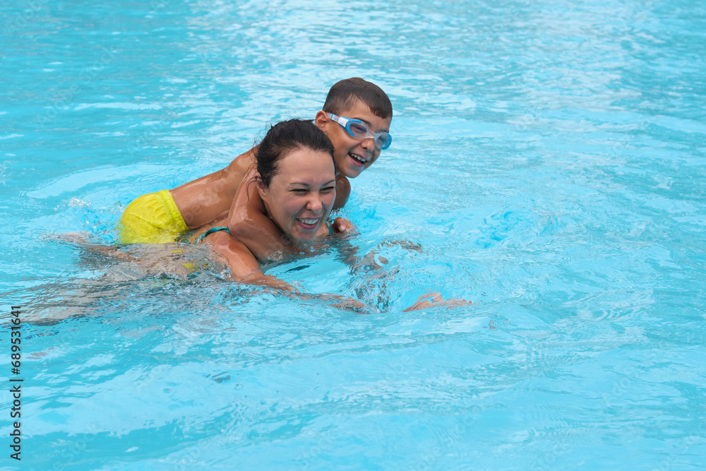 Vacation joy as mom and boy swim; true happiness. Reflects the growing trend of experiential family travel.