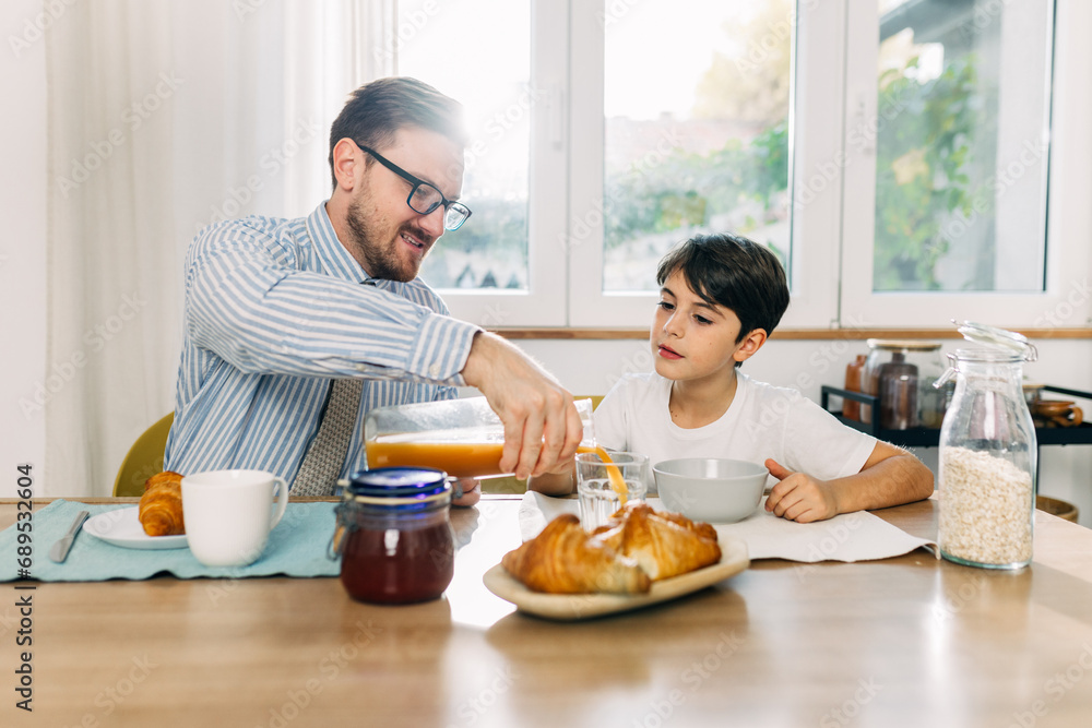 Father is pouring juice for his son during breakfast. Father is pouring juice for his son during breakfast.
