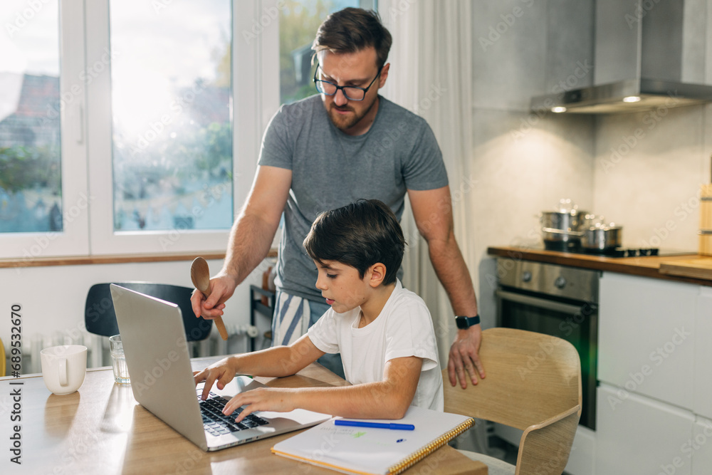 Obraz premium Father is helping his son use the laptop while cooking.