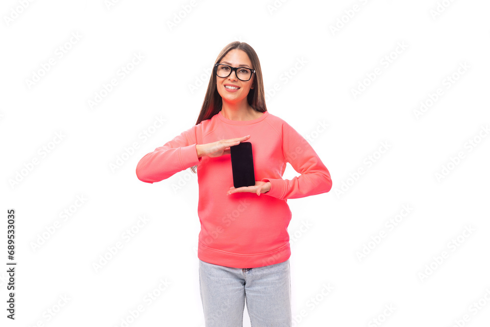 portrait of a young pretty european model woman with long black hair dressed in a pink sweater holding a phone vertically with a mockup on a white background with copy space portrait of a young pretty european model woman with long black hair dressed in a pink sweater holding a phone vertically with a mockup on a white background with copy space