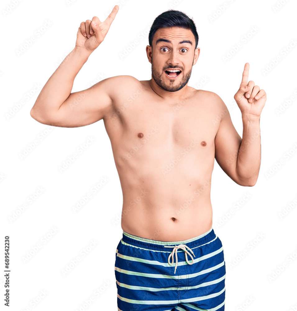 Young handsome man wearing swimwear smiling amazed and surprised and pointing up with fingers and raised arms. Young handsome man wearing swimwear smiling amazed and surprised and pointing up with fingers and raised arms.
