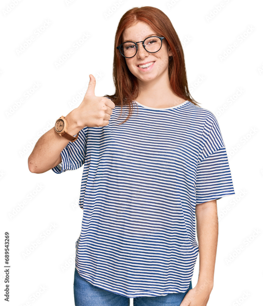 Young read head woman wearing casual clothes and glasses doing happy thumbs up gesture with hand. approving expression looking at the camera showing success. Young read head woman wearing casual clothes and glasses doing happy thumbs up gesture with hand. approving expression looking at the camera showing success.