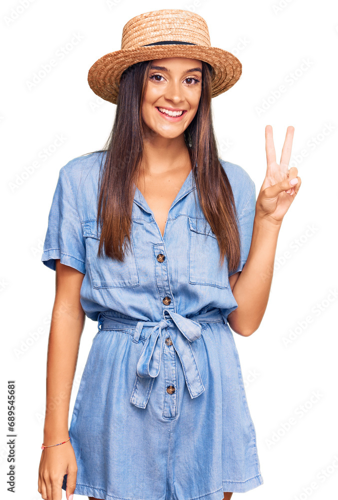Young hispanic woman wearing summer hat smiling with happy face winking at the camera doing victory sign. number two. Young hispanic woman wearing summer hat smiling with happy face winking at the camera doing victory sign. number two.