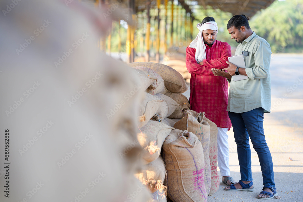 An expert from the agriculture sector checks the grains available in the food grain market and provides information about the crop to the farmer on a tablet.