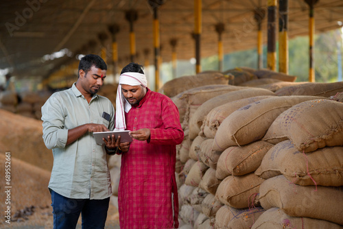 An expert from the agriculture sector checks the grains available in the food grain market and provides information about the crop to the farmer on a tablet.