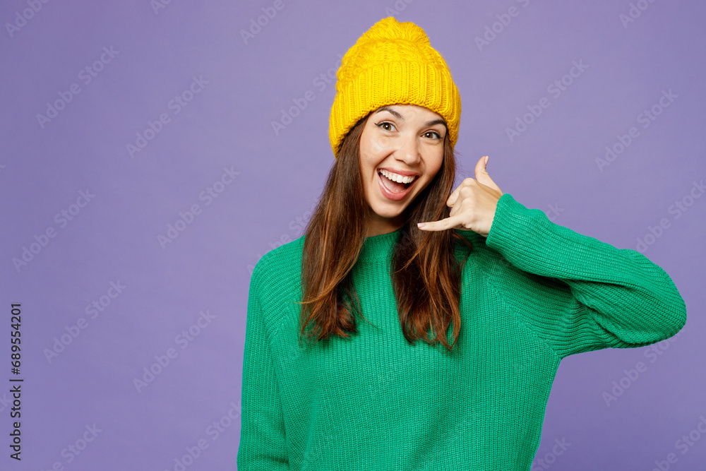 Young excited happy woman wear green sweater yellow hat casual clothes doing phone gesture like says call me back isolated on plain pastel light purple background studio portrait. Lifestyle concept. Young excited happy woman wear green sweater yellow hat casual clothes doing phone gesture like says call me back isolated on plain pastel light purple background studio portrait. Lifestyle concept.