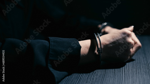 Female hands in handcuffs are leaning on a table in an interrogation room  close-up