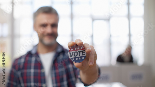 Slika na platnu A smiling middle-aged man holding out a vote button on camera, asserting his vot