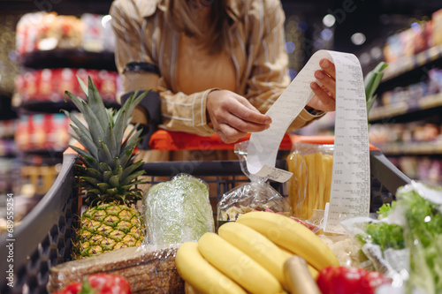 Cropped young customer woman wear casual clothes read check bill shopping at supermaket store grocery shop buying with trolley cart choose products in hypermarket. Purchasing food gastronomy concept.