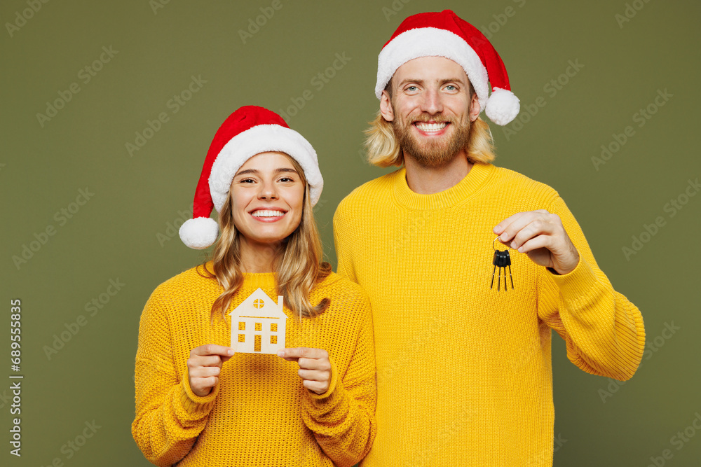 Merry smiling young couple two friends man woman wear sweater Santa hat posing hold keys wooden mockup of house isolated on plain green background Happy New Year celebration Christmas holiday concept Merry smiling young couple two friends man woman wear sweater Santa hat posing hold keys wooden mockup of house isolated on plain green background Happy New Year celebration Christmas holiday concept
