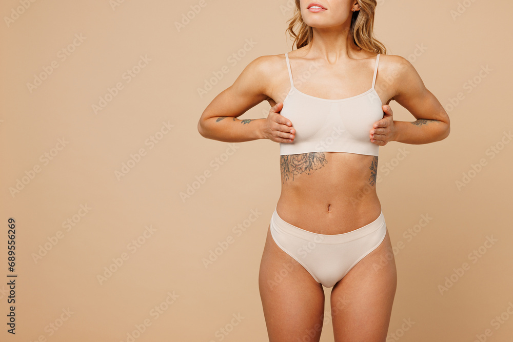 Naklejka premium Close up cropped young nice lady woman with slim body perfect skin wearing nude top bra lingerie stand holding put hand on breast chest isolated on plain beige background. Lifestyle diet fit concept.