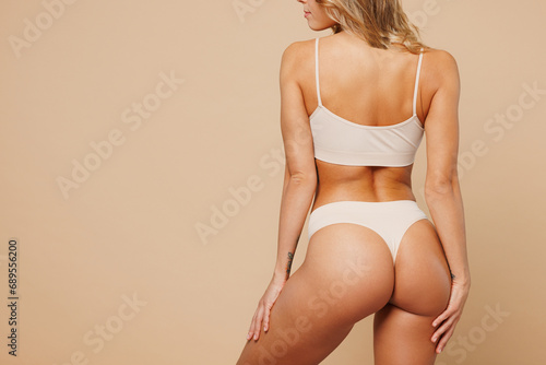 Foto Cropped back rear view young nice lady woman with slim body perfect skin wear nude top bra lingerie stand holding hands on thighs isolated on plain pastel beige background