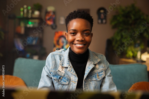 Portrait of delighted afro american woman in casual denim outfit smiling at camera sitting in frontof computer working from distance online. photo