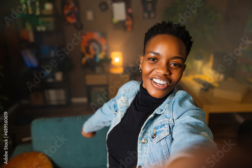 Cheerful african american woman takes selfie standing in the living room smiling wearing casual denim outfit.