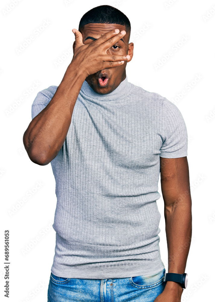 Young black man wearing casual t shirt peeking in shock covering face and eyes with hand, looking through fingers with embarrassed expression. Young black man wearing casual t shirt peeking in shock covering face and eyes with hand, looking through fingers with embarrassed expression.