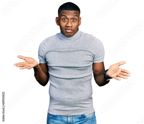 Young black man wearing casual t shirt clueless and confused with open arms, no idea concept.