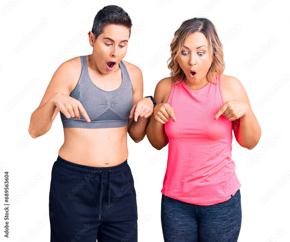 Couple of women wearing sportswear pointing down with fingers showing advertisement, surprised face and open mouth Couple of women wearing sportswear pointing down with fingers showing advertisement, surprised face and open mouth