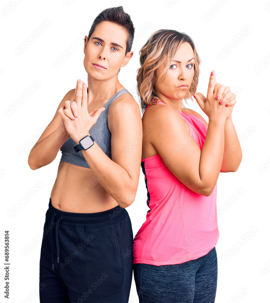 Couple of women wearing sportswear holding symbolic gun with hand gesture, playing killing shooting weapons, angry face Couple of women wearing sportswear holding symbolic gun with hand gesture, playing killing shooting weapons, angry face