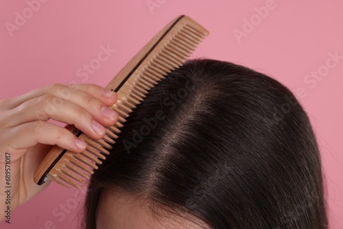 Woman with comb examining her hair and scalp on pink background, closeup