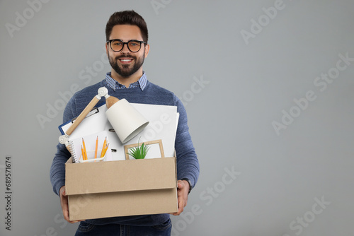 Happy unemployed man with box of personal office belongings on light grey background. Space for text photo