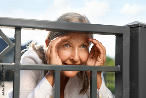 Concept of private life. Curious senior woman spying on neighbours over fence outdoors