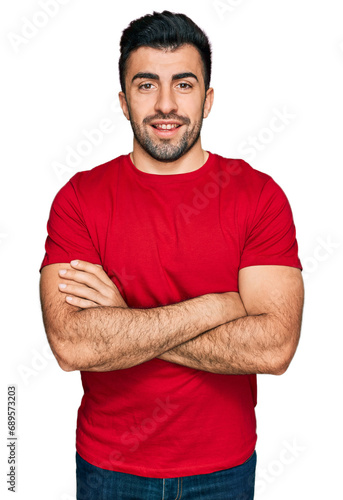 Hispanic man with beard wearing casual red t shirt happy face smiling with crossed arms looking at the camera. positive person.
