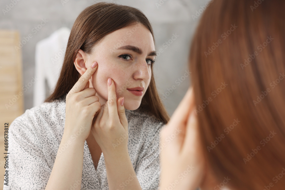 Young woman with skin problem looking at mirror indoors Young woman with skin problem looking at mirror indoors