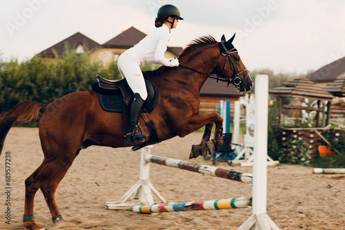 Side view of dressage horse jump barrier with female rider jockey in white uniform during jumping competition © primipil
