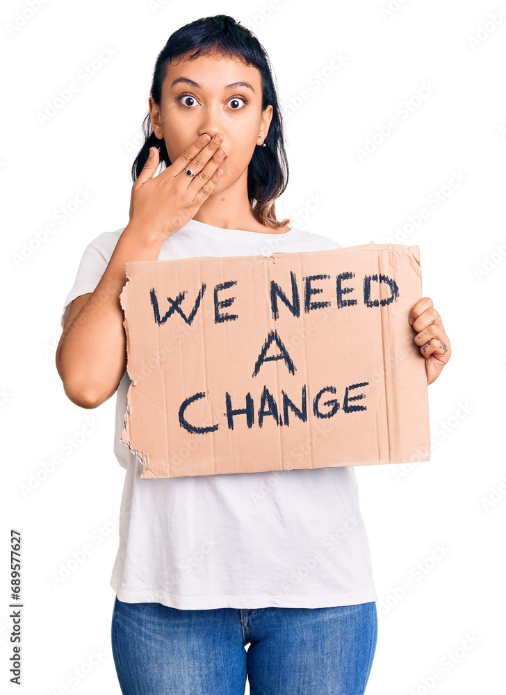 Young woman holding we need a change banner covering mouth with hand, shocked and afraid for mistake. surprised expression Young woman holding we need a change banner covering mouth with hand, shocked and afraid for mistake. surprised expression