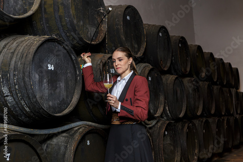 Focused young woman venenciador pouring wine with venencia into glass in cellar photo
