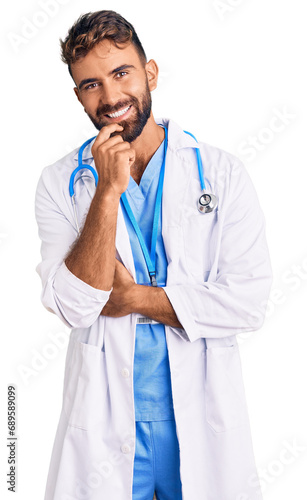 Young hispanic man wearing doctor uniform and stethoscope looking confident at the camera with smile with crossed arms and hand raised on chin. thinking positive.