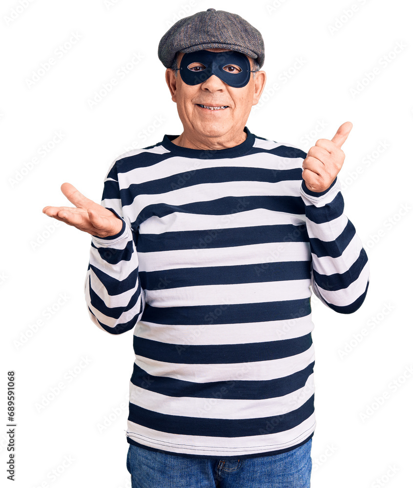 Senior handsome man wearing burglar mask and t-shirt showing palm hand and doing ok gesture with thumbs up, smiling happy and cheerful Senior handsome man wearing burglar mask and t-shirt showing palm hand and doing ok gesture with thumbs up, smiling happy and cheerful