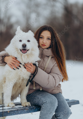 Fototapeta Naklejka Na Ścianę i Meble -  A girl walks with her beloved pet Samoyed in winter on the shore of a lake in the park.
