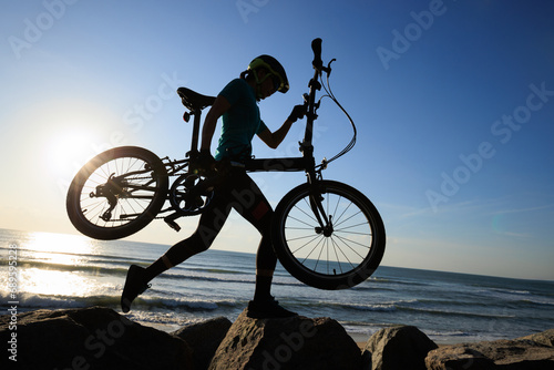 Woman carrying a folding bike on sunrise seaside
