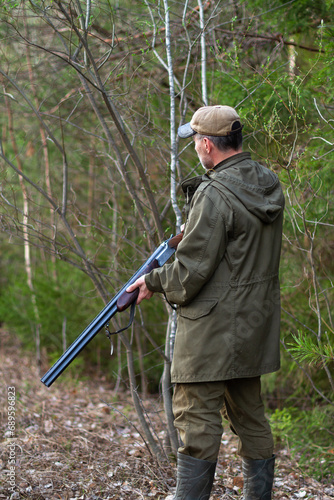 a hunter stands with a shotgun at the ready in a forest clearing