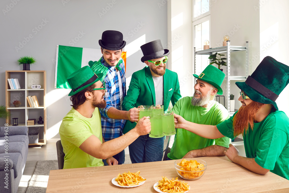Happy friends celebrating St Patrick's Day. Group of Irish men in leprechaun hats having a party, sitting at table with chips and French fries, saying toast, clinking big mugs, and drinking green beer - obrazy, fototapety, plakaty 