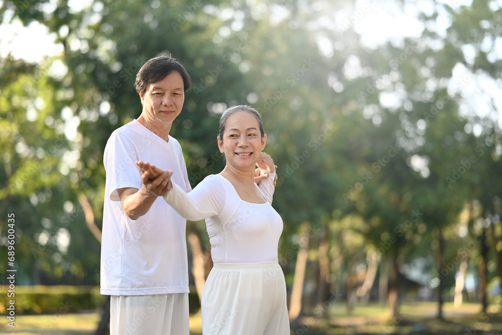 Active middle aged couple practicing Tai Chi Chuan in the park with sunrise. Mental health and wellbeing concept